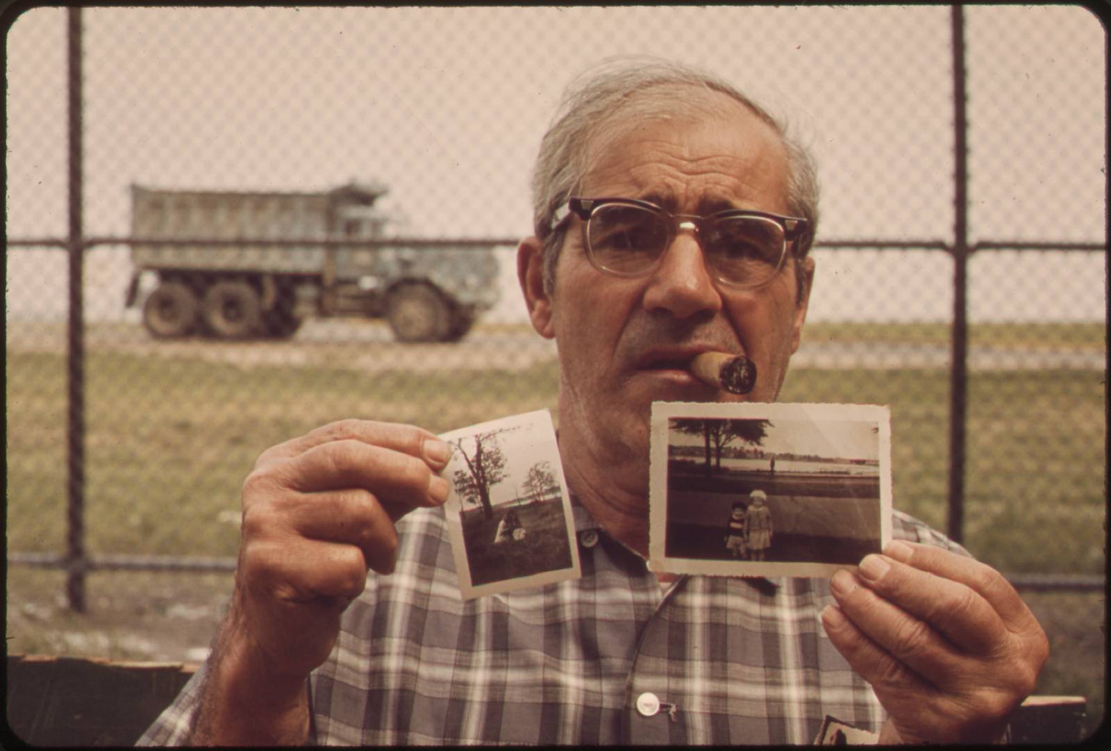 East Boston, 1973: Matthew Vieira holds up two small faded prints of his children, photographed decades earlier in the park where he stands — the park itself is now gone.